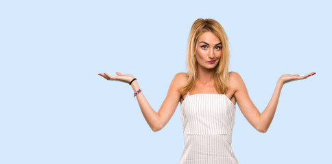 Fototapeta na wymiar Young blonde woman having doubts while raising hands over isolated blue background