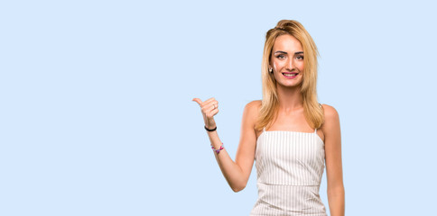 Fototapeta na wymiar Young blonde woman pointing to the side to present a product over isolated blue background