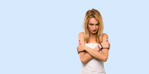 Young blonde woman freezing over isolated blue background