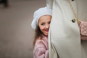 Cute girl in beret and coat hiding behind mom