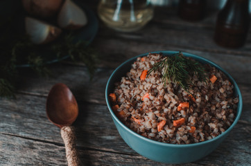 Buckwheat porridge with carrots on an old rustic, wooden background. Cutlery, oil bottle, dill, pepper and salt shaker, onion.
