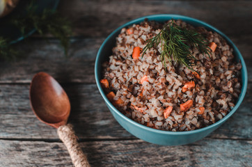 Buckwheat porridge with carrots on an old rustic, wooden background. Cutlery, oil bottle, dill, pepper and salt shaker, onion.