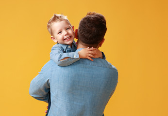 happy father's day! cute dad and son hugging on yellow background.