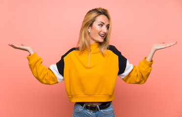 Young blonde woman over isolated pink background holding copyspace with two hands