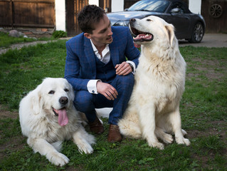 Elegant young handsome man in blue costume play with Tatra Shepherd Dog outdoor.