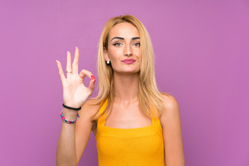 Young blonde woman over purple background showing an ok sign with fingers