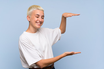 Teenager girl with white short hair over blue wall holding copyspace to insert an ad