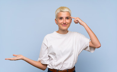 Teenager girl with white short hair over blue wall making the gesture of madness putting finger on...