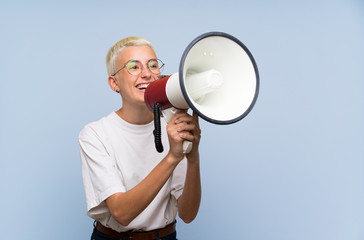 Teenager girl with white short hair over blue wall shouting through a megaphone
