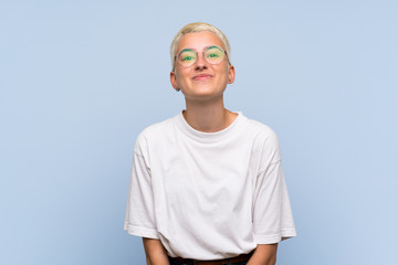 Teenager girl with white short hair over blue wall with glasses and smiling