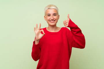 Teenager girl with white short hair over green wall showing ok sign and thumb up gesture