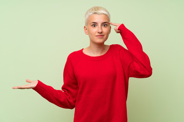 Teenager girl with white short hair over green wall making the gesture of madness putting finger on...