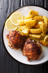 Traditional Greek Lemon Garlic Roasted Potatoes (Patates fournou)  with grilled chicken thighs on a plate close-up. Vertical top view