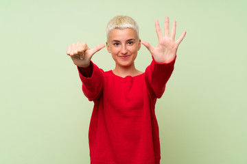 Teenager girl with white short hair over green wall counting six with fingers