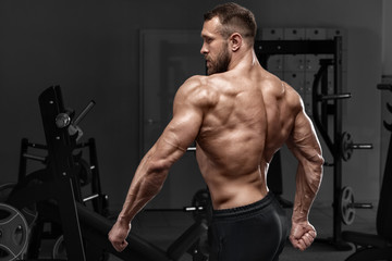 Obraz na płótnie Canvas Rear view muscular man showing back muscles at the gym. Strong male naked torso, workout