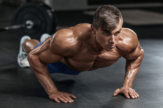 Muscular man working out in gym doing push-ups exercises, strong male naked torso abs