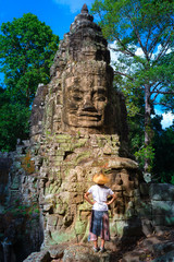 Woman in Bayon Temple looking at stone faces, Angkor Thom, morning light clear blue sky. Buddhism meditation concept, world famous travel destination, Cambodia tourism.
