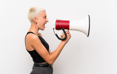 Teenager girl with short hair over white wall shouting through a megaphone
