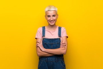 Teenager girl with overalls on yellow background keeping the arms crossed in frontal position