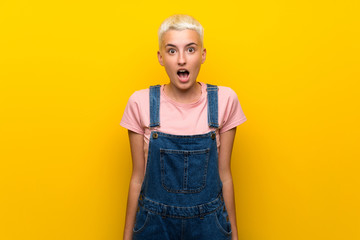 Teenager girl with overalls on yellow background with surprise facial expression