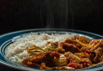 Hot rice, chicken vegetable served on a blue plate with hot steam black background