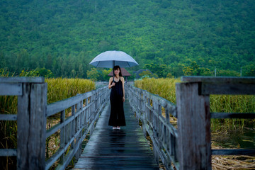 Black dress woman standing alone on a walkway with an umbrella in a rainy day