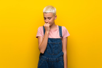 Teenager girl with overalls on yellow background having doubts