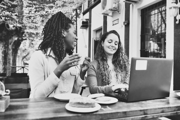 Working meeting between two young women in front of a café, with laptop and mobile