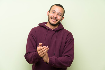 Colombian man with sweatshirt over green wall applauding