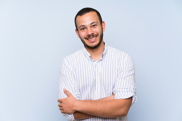 Colombian man over isolated blue wall keeping the arms crossed in frontal position