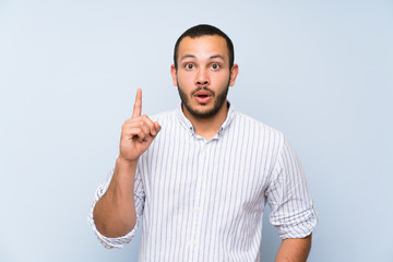 Colombian man over isolated blue wall thinking an idea pointing the finger up