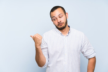 Fototapeta premium Colombian man over isolated blue wall unhappy and pointing to the side
