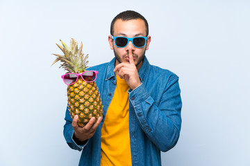 Colombian man holding a pineapple with sunglasses showing a sign of closing mouth and silence...