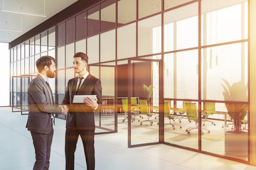 Two businessmen shaking hands near meeting room