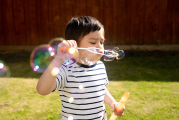 Happy boy blowing soap bubbles in the garden,Cute 4 years old kid blowing bubble wand with a funny face,Cute kid playing in the garden on a sunny summer day,Outdoor activities for Children