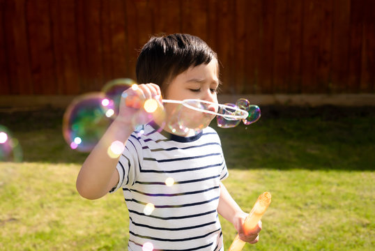 Happy boy blowing soap bubbles in the garden,Cute 4 years old kid blowing bubble wand with a funny face,Cute kid playing in the garden on a sunny summer day,Outdoor activities for Children