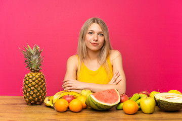 Young blonde woman with lots of fruits keeping arms crossed