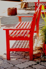Bright red wooden benches stand on the street, covered with paving stones. It's summer outside.