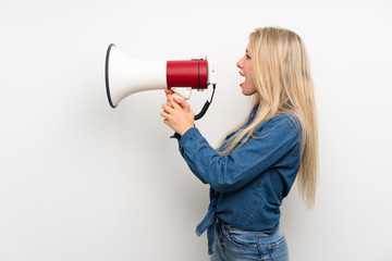 Young blonde woman over isolated white wall shouting through a megaphone
