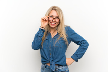 Young blonde woman over isolated white wall with glasses and smiling