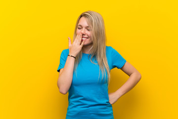 Young blonde woman over isolated yellow background smiling a lot