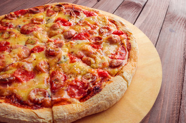 tasty pizza with  cheese sausage tomatoes on round cutting board close up