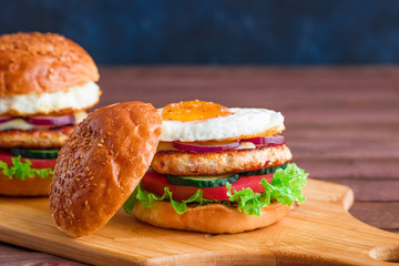 burgers with chicken cutlet fried egg tomato lettuce cucumber on cutting board