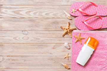 Top view of Beach flat lay accessories. sunscreen bottle with seashells, starfish, towel and flip-flop on wooden board background with copy space