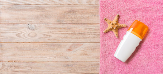 Beach flat lay accessories with copy space. Pink towel, starfish and a bottle of sunblock on wooden background. Summer holiday concept