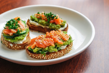 open sandwiches with salmon cucumber mashed avocado red onion dill on white plate