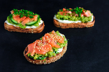 open sandwiches with salmon avocado cucumber dill sesame seeds on black background