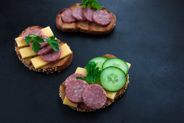 open sandwiches  with rye bread  salami cheese cucumber and parsley  on black background copy space