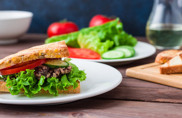 sandwich with tuna  bread  lettuce tomato cucumber on white plate soft focus