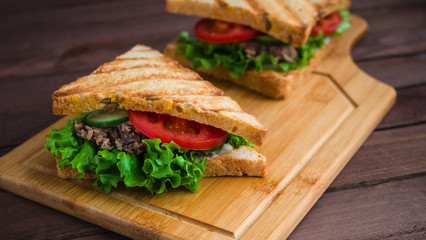 sandwiches with grilled bread tuna lettuce tomato cucumber on wooden cutting board close up